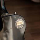Detail zadní strany černé kytary s kovovým krytem v oblasti konece hředu. Na zlatém nápisu je uvedeno Gibson CUSTOM a pod ním na kovovém prstenci tex…