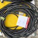 Černý kabel sletovaný v klubku, zakončený konektory typu XLR. Na kabelu je připevněna bílá papírová štítková nálepka s červeným okrajem, na které je…