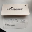 Fotografie zobrazuje dvě papírové štítky. Horní bílý štítek nese černé logo Harmony a nápis SINCE 1892. Spodní štítek obsahuje tabulku s políčky Wood…
