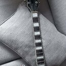 Kytara s tmavým, pravděpodobně černým lakem a bílými lemováním. Na hlavě je viditelný nápis GRETSCH. Hmatník má bílé blokové vložky a je vidět šest l…