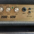 Detail kytarového zesilovače se zlatým předním panelem. Na panelu je nápis JCM 2000 - 60W a podpis Jim Marshall. Jsou zde ovládací knofíky s popisky…