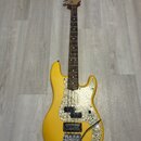 Žlutá elektrická basová kytara s hnědým hnedým hnedým hradlem a perleťovým pickguardem. Na hlavě nástroje je viditelné logo Fender. Kytara má dva sní…
