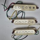 Tři krémově bílé snímače pro elektrickou kytaru s šesti kovovými póly. Každý snímač má v levé části nápis NPS a je vybaven připojovacími vodiči v růz…