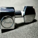 Kryt ladicího kolíku z chromovaného kovu s hranatým tvarem. Na čele je vyryté logo Fender v kruhu. Povrch je lesklý s viditelnými drobnými škrábancem…