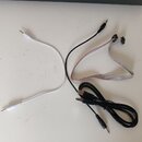 Na bílém podkladu jsou položeny tři kabely. Jeden je bílý s konektory jack na obou koncích, druhý je černý s konektorem jack a USB, a třetí je plochý…