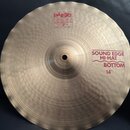 Kruhové činely z mosazi s jemným rýhováním povrchu. Na číneli jsou červené nápisy PAiste 2002 MADE IN SWITZERLAND a SOUND EDGE HI-HAT BOTTOM 14". Okr…