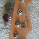 Hlava basové kytary z přírodního dřeva s čtyřmi chromovanými ladičkami. Na povrchu je černý nápis Fender JAZZ BASS® a menší text MADE IN U.S.A. Povrc…