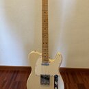 Elektrická kytara typu Telecaster v krémové barvě s bílým pickguardem. Na hlavě hředu je viditelné logo Fender. Nástroj má javorový hmatník a kovové…