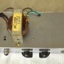 Elektronické zařízení v hliníkovém šasi s ovládacími prvky na přední straně. Na horní části jsou umístěny dva transformátory, z nichž jeden má žlutý…