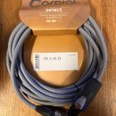 Šedý audio kabel s konektory, umístěný na oranžovém kartonovém podkladu. Na balení je logo CORDIAL a nápis select s textem Premium quality components…