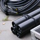Na fotografii jsou svazky černých a bílých kabelů s konektory. Na černém kabelu je viditelný nápis „10 GbR S/STP 4x26AWG26 by SOMMER CABLE Germany“.…