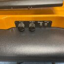 Detail ovládacího panelu žlutého nástroje. Na černém panelu jsou dva černé otočné knoflíky s nápisy Volume a Sub Bass, vstupní zásuvka Mp3 in a výstu…