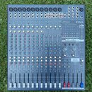 Šedý mixovací pult značky YAMAHA s označením modelu EMX5016cF. Zařízení obsahuje více vstupních kanálů s posuvníky, řadu otočných knoflíků v různých…