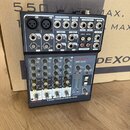 Černý mixážní pult s nápisem DEXON DMC 2220 a popiskem 2 mono + 2 stereo channel mixer. Horní panel obsahuje různé vstupy a výstupy, včetně konektorů…