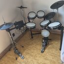 Elektronická bicí souprava s černým rámem a bílými bubnovými plochami. Souprava obsahuje pět padů, tři činely a ovládací modul s nápisem Roland. K sa…