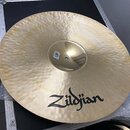 Zlatý kovový činel s jemným rýhováním po celém povrchu. Na spodní části je černým nápisem uvedena značka Zildjian. V centru činelu je vidět malá bílá…