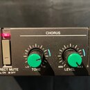Černý efektový pedál s nápisem CHORUS. Obsahuje dva zelené otočné oválné knoflíky s popisky TONE (rozsah LO až HI) a LEVEL (rozsah MIN až MAX). Vlevo…