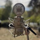 Kondenzátorový mikrofon v kovovém provedení s matným povrchem, umístěný v odpruženém držáku (shock mount). Na těle mikrofonu je štítek s nápisy: Mode…