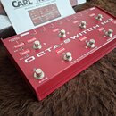 Červený přepínač s nápisem OCTA-SWITCH MK3 a doplňkovými texty EXTERNAL SWITCH, EXT., EXT. 2, OUTPUT, BYPASS a MADE BY EAST SOUND DENMARK DESIGNED BY…