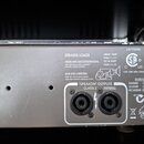 Zadní strana šedého elektronického zařízení s dvěma SpeakON konektory. Na povrchu je text „SPEAKER LOADS“, „480W AMP (WOOFER/MASTER)“, „50W AMP (TWEE…