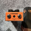Oranžový kytarový efekt pedál značky tc electronic. Na boku jsou vidět konektory INPUT a OUTPUT, napájecí vstup s nápisem 9 V DC 100 mA a symbol pola…