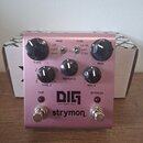 Růžový kytarový efekt s nápisy DIG, dual digital delay a strymon. Na horní straně jsou čtyři otočné ovladače s popisky TIME, REPEATS a MIX, dvěma řad…