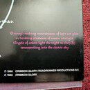 Detail zadní strany obalu CD nebo vinylové desky s černým povrchem. Uprostřed je růžový text v kurzívě: „Through arching moonbeams of light we glide…