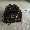 Černý elektronický přístroj s kovovou mřížkou na horní straně. Na zadní straně jsou viditelné nápisy BYPASS, DARK a konektory s popisky PHONES, OUTPU…