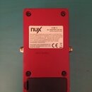 Zadní strana červeného kytarového efektu v kovovém šasi. Na povrchu je bílý nápis s logem nux, údajem AC ADAPTER: DC 9V a webovou adresou www.nuxefx.…