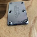 Kryt hnízda krakového šejku z chromovaného kovu připevněný šesti šrouby na světlém dřevě. Na povrchu je vyražen nápis ERNIE BALL MUSICMAN a sériové č…
