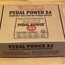 Kartonová krabice s nápisem VOODOO LAB PEDAL POWER X4 COMPACT ISOLATED DC POWER SUPPLY. Na horní straně je obrázek produktu s texty HYBRID DC TRANSFO…