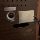 Detail zadní strany hnědého hudebního přístroje s dřevěnou strukturou. Na bílém štítku je nápis MANUFACTURED BY FARFISA, a subsidiary of Lear Siegler…