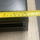 Detailní záběr na hranu černého elektronického zařízení z kovového materiálu. Přes horní hranu je přiložen žlutý skladací metr, který ukazuje rozměr.…