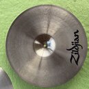 Kruhové činely z kovu s viditelným broušením povrchu. Na pravé straně je černý nápis Zildjian. V centru se nachází malá bílá nálepka s nečitelným tex…