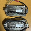 Dva kytarové humbuckery s kovovým krytem a připojenými kabely. Horní snímač má štítek s nápisy HB102B/CRC, BRIDGE a 1102. Dolní snímač má štítek s ná…