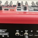 Detail zadní strany červeného klavíru s ovládacími prvky na horním panelu. Na zadním černém panelu jsou viditelné konektory s nápisy ROTOR PEDAL, USB…