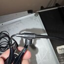 Černý mikrofon s připevněnou svorkou a kabelovkou. Na těle mikrofonu je bílý nápis MG7 a pod ním menší text MADE IN JAPAN. Povrch je matně černý, bez…