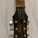 Detail hlavy černé kytary s hnedým hmatníkem. Na hlavě jsou bílé nápisy „GIBSON“, „Special MODEL“ a logo „Epiphone“. Jsou vidět šest chromovaných lad…