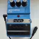 Modrý kytarový efekt s třemi černými oválovými knoflíky popsanými jako DELAY, MIX a REPEAT. Na přední straně je bílý nápis FX 90 Delay a stříbrný ští…
