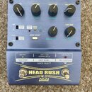 Modrý efektový pedál s nápisem HEAD RUSH a logem AKAI professional. Zařízení má čtyři černé otočné knoflíky (LEVEL, FEEDBACK, TIME a TIME FINE), červ…