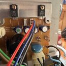 Fotografie zachycuje detail elektronické desky s komponenty. Jsou zde vidět dva černé tranzistory přišroubované k kovovému chladiči, z nichž jeden má…