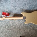Zadní strana elektrické kytary v krémové barvě s jasným lakem. Na hmatníku je vidět nápis "Fender" a na kovovédesce u krku je logo s nápisem "Fender"…