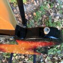 Detail zadní strany kytary s červeno-žlutým přechodem barev (sunburst) a černým okrajem. Na kovovém šperku je viditelný nápis MADE IN JAPAN. V horní…