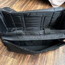 Černá látková přepravní taška s otevřeným zipem. Vnitřek je vyložen černé polstrováním s několika oddělovači a má dvě přšívané úchytky. Na fotce nejs…