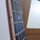 Detail hředu elektrické kytary s tmavým hmatníkem a bílými tečkovými značkami poloh. Na hraně hmatníku je vidět světlá vrstva (binding) a červený lak…