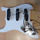 Bílá pickguard pro elektrickou kytaru s třemi černými snímači typu single-coil. K snímačům vedou bílé a černé vodiče, které jsou připojeny k elektron…