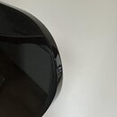 Detailní záběr na černý, lesklý povrch hudebního nástroje nebo příslušenství. Povrch má jemnou metalickou texturu s viditelnými odlesky. Na spodní čá…