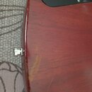 Detail červeného lakovaného těla kytary s černým plechtrátem. Na povrchu laku jsou viditelné škrábance a světlejší oděrka v dolní části. V levé části…