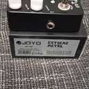 Černý kytarový efekt s bílými ovládacími knoflíky a dvěma stoupacími spínači. Na horní straně je bílý nápis EXTREME METAL a logo JOYO. Vedle efektu j…