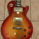 Elektrická kytara s tvarem singlecut a povrchovou úpravou v červeno-žlutém gradientu (sunburst). Nástroj má dva humbuckery s kovovými kryty, čtyři ot…